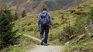 Ein Mensch wandert einen Weg lang und hat einen Rucksack dabei.