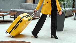 Eine Frau zieht einen Gelben Koffer hinter sich her durch eine Hotellobby