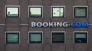 Eine Hauswand mit 8 Fenstern und in der Mitte steht "Booking.com".