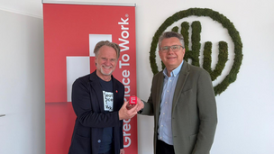 Zwei lachende Männer im Jackett vor Logos 