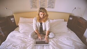 Eine Frau sitzt auf einem Bett an ihrem Laptop