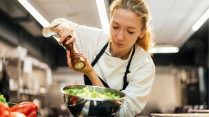 Junge Köchin würzt Salat in einer professionellen Hotelküche