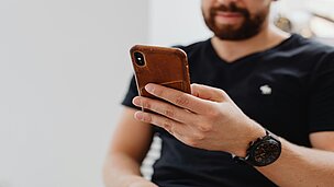 Mann mit Vollbart hält Handy mit brauner Lederhülle