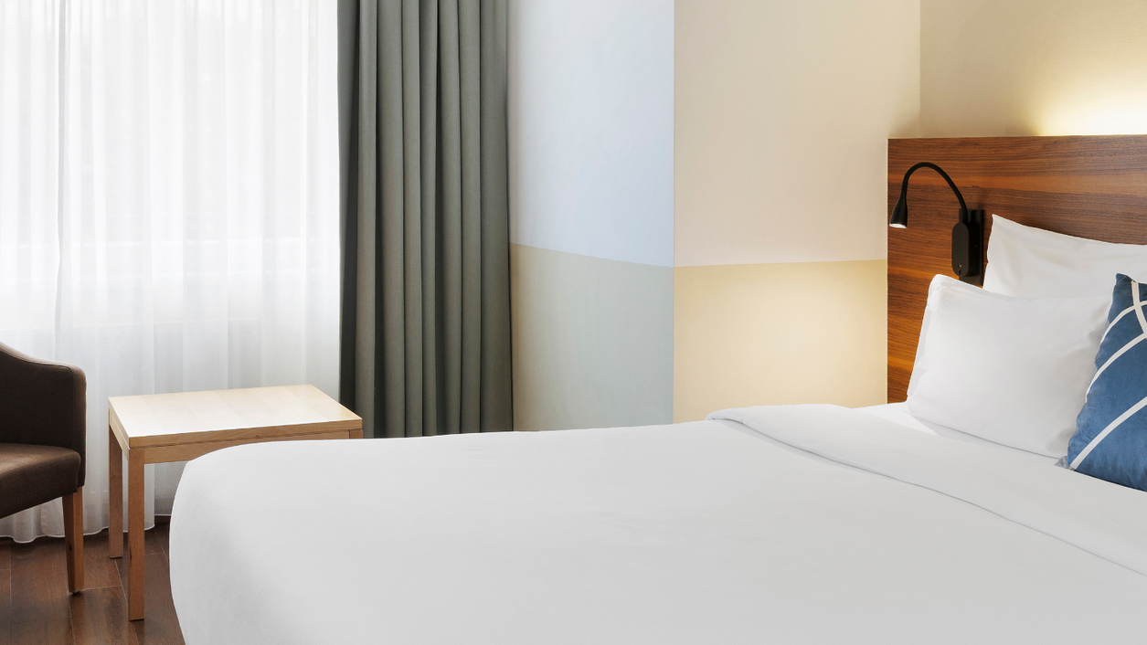 Hotelzimmer mit weiß bezogenem Bett und grünem Vorhang