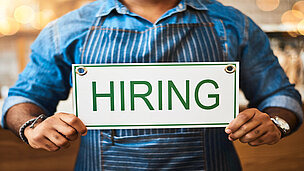 Jemand hält ein Schild in der Hand wo: "HIRING" draufsteht