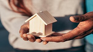2 Hände mit kleinem Holzhaus