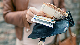 Hand greift in Geldbörse und nimmt Geld heraus