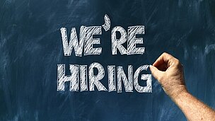 Hand schreibt auf Tafel we're hiring
