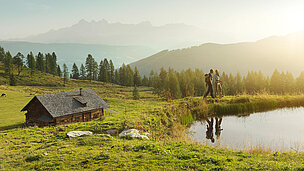 Bergsee mit Hütte und einem Pärchen das wandert 