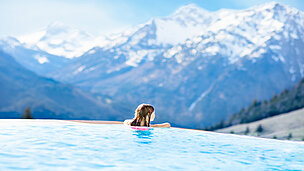 Ein Kind ist im Pool und guckt in Richtung der Berge.