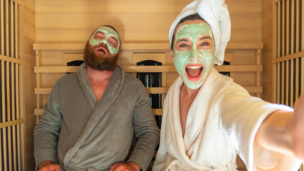 Frau mit Gesichtsmaske, die ein Selfie mit einem schlafenden Mann (auch mit Gesichtsmaske) macht