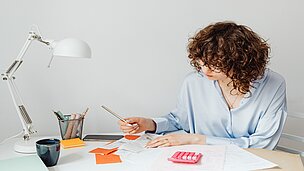Frau rechnet am Schreibtisch mit einem Taschenrechner