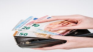 Eine Hand tut Geldscheine in ein Portmonnaie