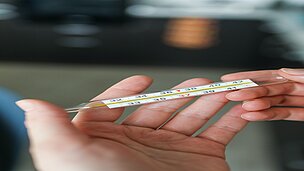 In einer Hand ist ein Fieberthermometer.