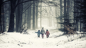 Drei Kinder laufen durch einen verschneiten Wald